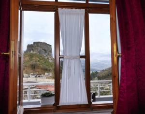 a window with a white curtain and a mountain view at Hotel Brahimi in Gjirokastër