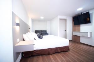 a bedroom with a white bed and a flat screen tv at Hotel Cisne in Cuenca