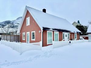 a red house in the snow with a white fence at Arctic Getaway Sørvågen - King Crab Welcome Gift in Sørvågen
