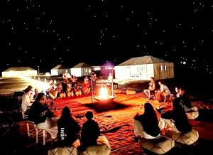 a group of people sitting around a fire at night at Sahara Imperial Luxury Camp in Merzouga