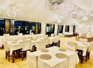a restaurant with white tables and chairs and windows at Sahara Imperial Luxury Camp in Merzouga