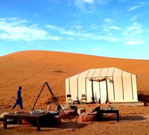 a man walking past a tent in a desert at Sahara Imperial Luxury Camp in Merzouga
