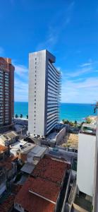 a tall white building with the ocean in the background at Quarto triplo em Petrópolis in Natal