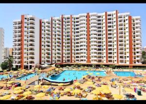 a large hotel with a swimming pool with umbrellas and people at Rocha Paradise Apartment in Portimão