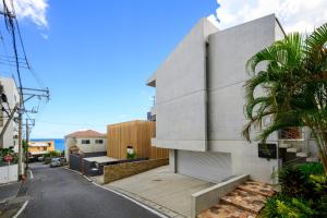 a white block building on a street with a palm tree at onna resort nakadomari ビーチまで車で4分 最大8名OK 中庭付き貸切ヴィラでくつろぐ恩納村ステイ in Onna