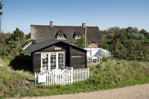 a small house with a white fence in front of a house at Charming Tiny House In Sønderho in Fanø