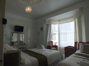 1 dormitorio con 2 camas, espejo y ventana en Taormina Guest House, en Tenby