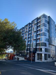 a tall white building on a street with a tree at Urba Residences in Auckland