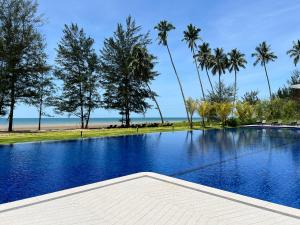 a swimming pool with palm trees and the beach at Roxy Beach Apartment, Sematan, Sarawak in Sematan