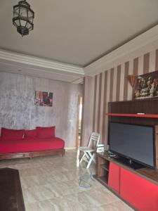 a living room with a red bed and a flat screen tv at Residence les jardins cap de l eau in Ras El Ma