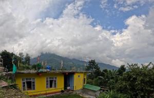 a yellow house with a mountain in the background at Hobo's Nest in Kurseong +13 photos