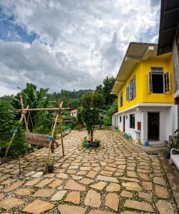 a yellow and white house with a stone patio at Hobo's Nest in Kurseong