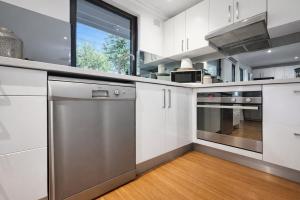 a kitchen with white cabinets and stainless steel appliances at Coastal Stay in Cronulla