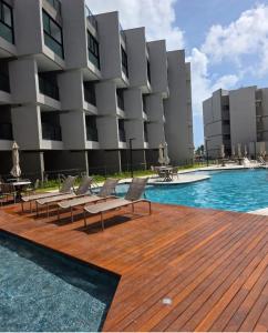 a swimming pool with chairs and a building at Beira mar Flat Deluxe Nomar Carneiros Ecoliving Réveillon in Tamandaré