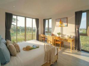 a bedroom with a bed and a desk and windows at Entire Hoi An Villas By Ovui in Hoi An