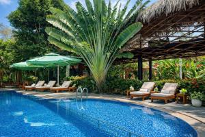 a pool with chairs and an umbrella and a palm tree at FORTUNE HOTEL 2 LUCKY STAY Phu Quoc in Phú Quốc