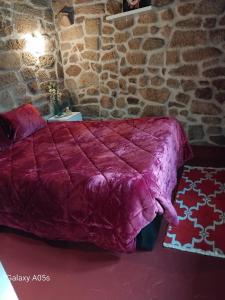 a red bed in a room with a stone wall at Casa Portela in Marialva