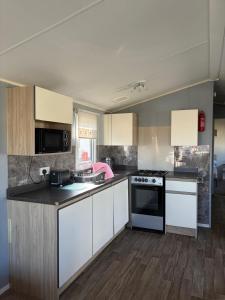 a kitchen with white cabinets and a stove at PG173 Golden Palm Resort 6 Berth Caravan With Decking in Chapel Saint Leonards