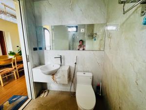 a man taking a picture of a bathroom with a toilet and sink at Mây Home Hoa Lư in Phúc Trì