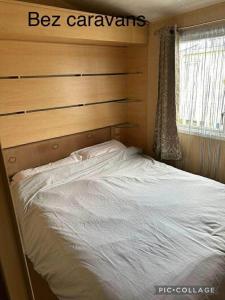 a bedroom with a white bed with a wooden headboard at Towyn Happy Days S7 in Rowen