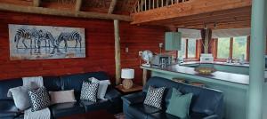 a living room with two black leather couches and a kitchen at Vaalkop Dam Reserve Log Cabin, Self-Catering, Beestekraal in Beestekraal