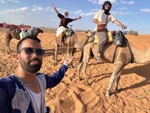 two people riding on camels in the desert at Achabou Desert Camp in Merzouga