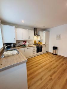 a kitchen with white cabinets and a wooden floor at Penuel 3-bedroom Retreat with workspace in Central Sutton-in-Ashfield in Sutton in Ashfield +27 photos