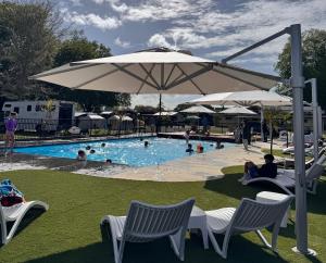 a pool with people sitting in chairs and an umbrella at Cambridge Top 10 Holiday Park in Cambridge
