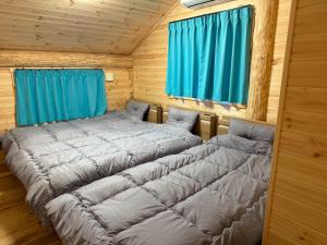 two beds in a wooden room with blue curtains at Villa Aso Otohime in Uchinomaki +4 photos