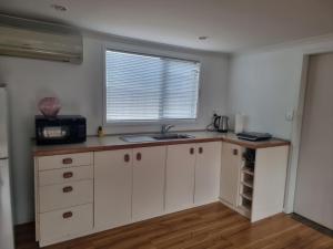 a kitchen with white cabinets and a sink and a window at Sailrock Studio in Mangawhai