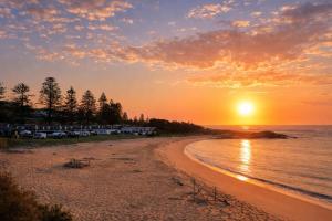 a beach with the sun setting over the water at Tuross Beach Cabins & Campsites in Tuross Heads