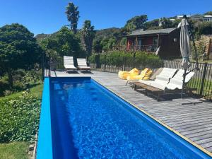 a swimming pool with chairs and an umbrella next to a house at Piha Tiny House in Piha
