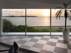a room with a view of the ocean and a palm tree at VOYAN Resort MiyakojimaーAZOMARE アゾマーレ in Miyako-jima