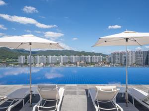two white chairs and umbrellas on a patio with the water at Chestertons Gyeongju in Gyeongju