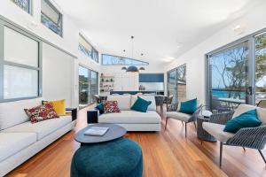 a living room with couches and chairs and windows at Architectural Beachfront Escape Yowani House in Tomakin +22 photos
