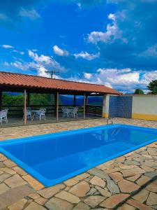 a blue swimming pool with a pavilion and tables and chairs at Pousada Pico do Papagaio in Aiuruoca