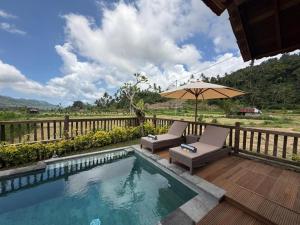 a swimming pool with two chairs and an umbrella at Kubu Sakian Villa and Restaurant Sidemen in Sidemen