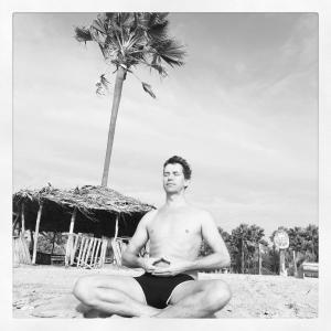 a man in a bathing suit sitting on the beach at Nemasu Eco-lodge in Gunjur