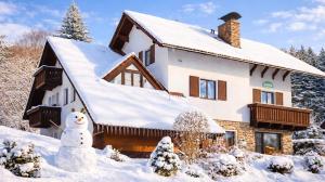 a house covered in snow with a snowman in front at Pension a apartmány Hanna in Železná Ruda