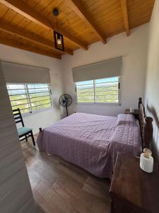 a bedroom with a bed and a chair and two windows at Las Pirquitas Villa Giardino in Huerta Grande