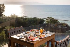 a table with plates of food on a balcony with the ocean at Anasa Luxury Resort in Elaiokhórion