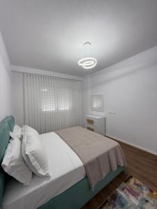 a white bedroom with a bed and a lamp at White Apartment in Kamëz