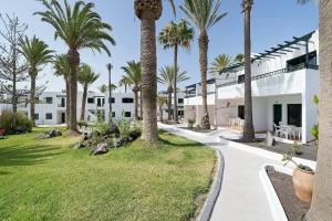 a walkway in front of a white building with palm trees at BLUESEA Playa Club in Puerto del Carmen