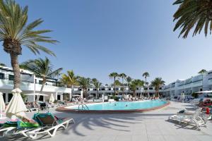 a pool at a resort with palm trees and chairs at BLUESEA Playa Club in Puerto del Carmen