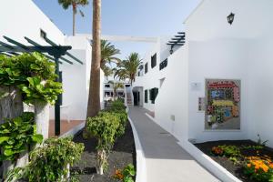 a hallway of a white building with trees and plants at BLUESEA Playa Club in Puerto del Carmen +21 photos