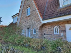 a brick house with a red roof and some bushes at Hues-Sylt in Morsum