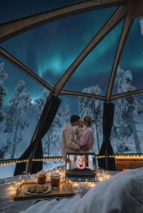 a couple kissing in front of a window with a laptop at Syöte Igloos in Syöte