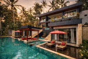 a house with a swimming pool with two chairs and an umbrella at Oran Villa Bali in Tampaksiring