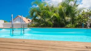 a blue swimming pool with palm trees in the background at Les Cannes Trankil in Saint-Louis