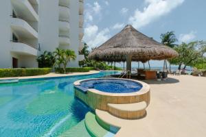 a swimming pool with a straw umbrella next to a building at Isla Condo Puerta al Mar 403 at Sac Bajo in Isla Mujeres